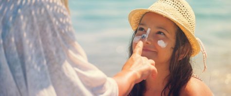 Young mother applying suntan lotion on daughters face at the beach